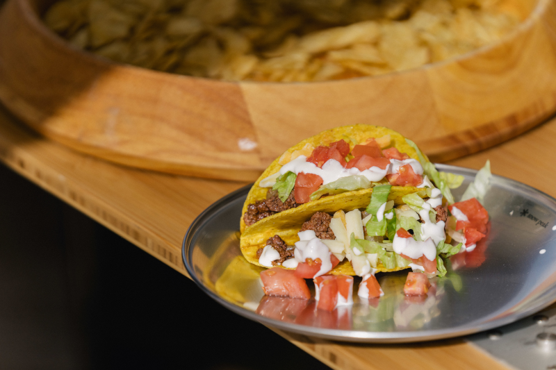 The Mirror Plate sits on a IGT Bamboo Extension with two hard tacos placed on top filled with ground beef, lettuce, tomatoes, and sour cream.