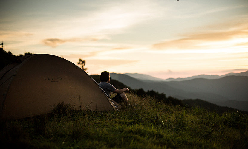 Person sitting in front of their tent overlooking a beautiful vista.