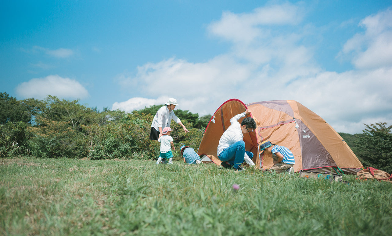 Image of a family setting up a tent in a large campfield under a blue sky.