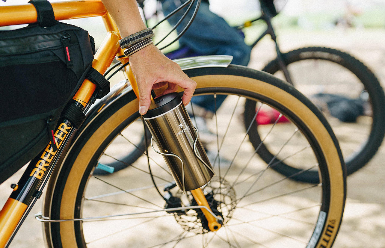 A person putting their Snow Peak Kanpai Bottle into a holder attached to a bicycle wheel.