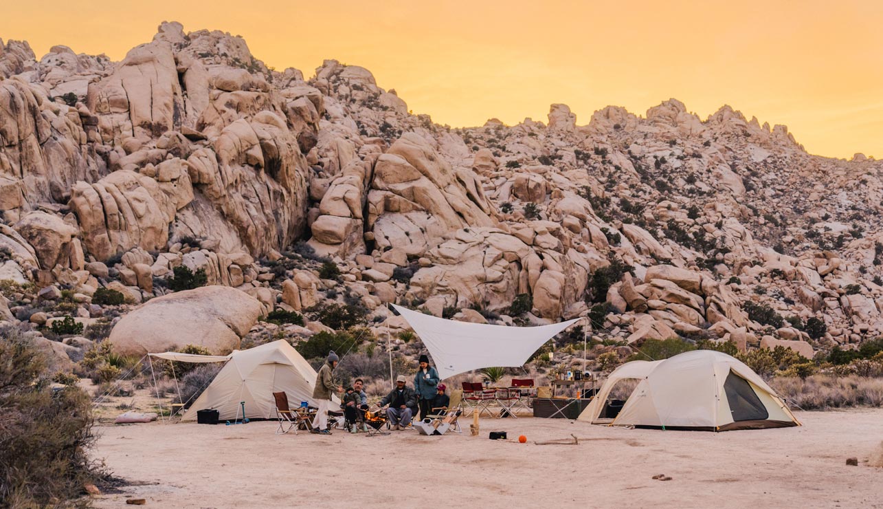 Image shows two tents and a tarp set up in front of a rocky bluff. 