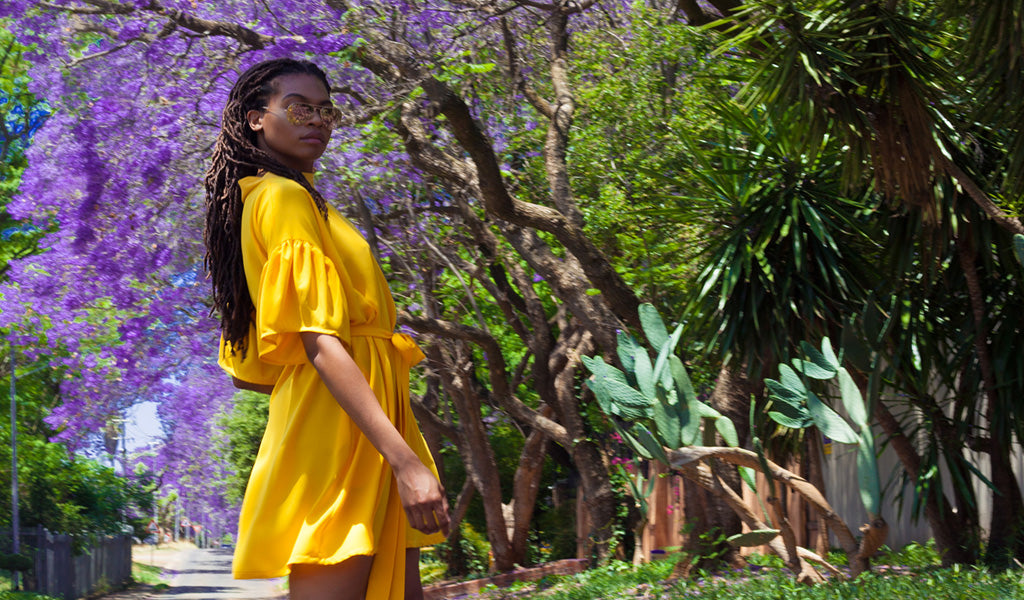 A model wearing a yellow dress against purple Jacaranda trees in Pretoria