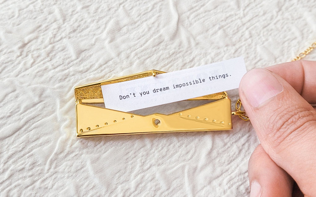 Hand holding a fortune over an envelope locket in front of a textured beige background.