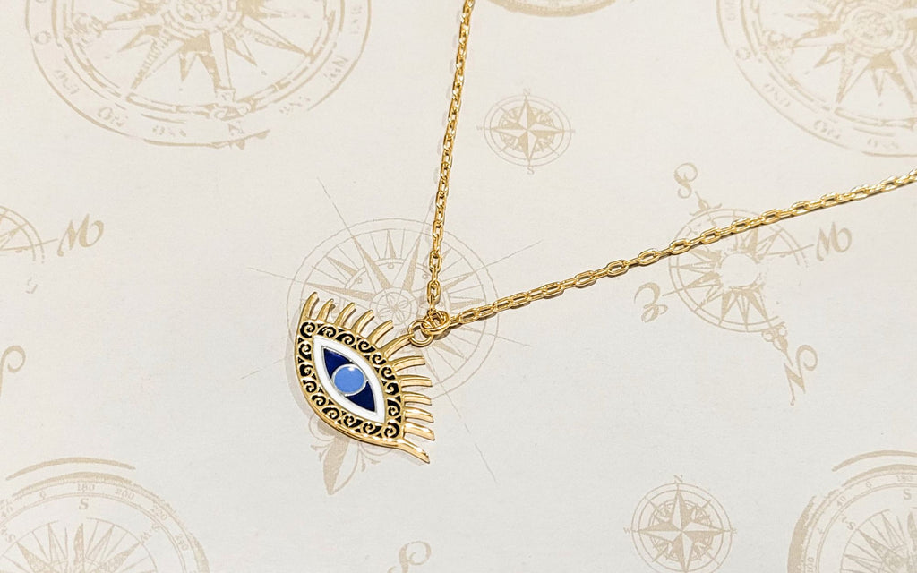 Evil eye necklace over a background with various pictures of compasses decorating it.