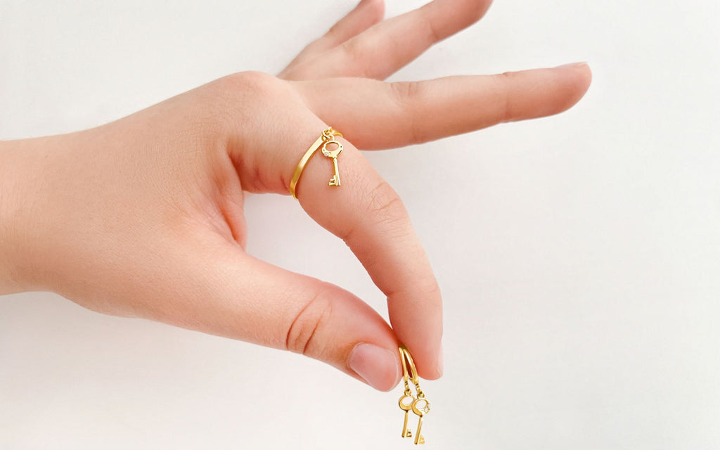 Hand holds Mini Key of F Earrings in between fingers while wearing a Key Charm Ring.