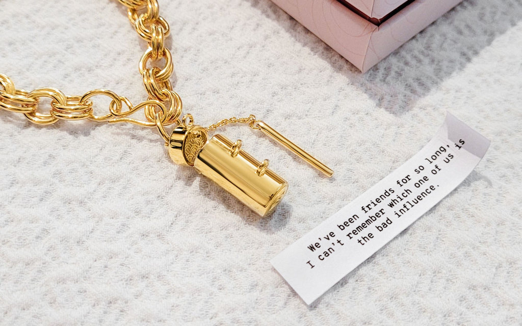 Capsule and wand bracelet with a fortune beneath and a corner of a box shown on top of a textured white background.