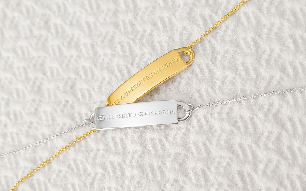 "Let yourself dream again" bracelets in gold and silver overlayed on top of each other in front of a white background