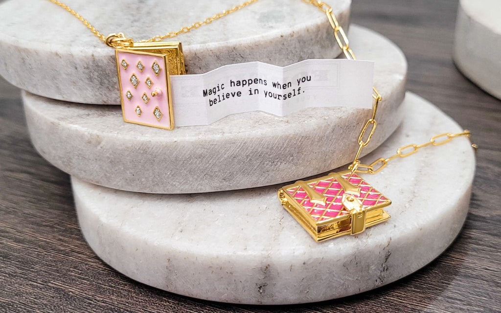 Two pink book lockets on top of round marble coasters with a fortune coming out of one book locket.
