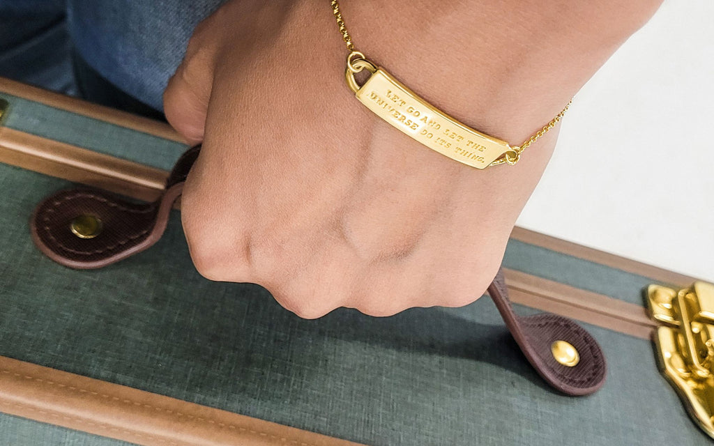 A hand holding the handle of an old school luggage wearing an engraved bracelet