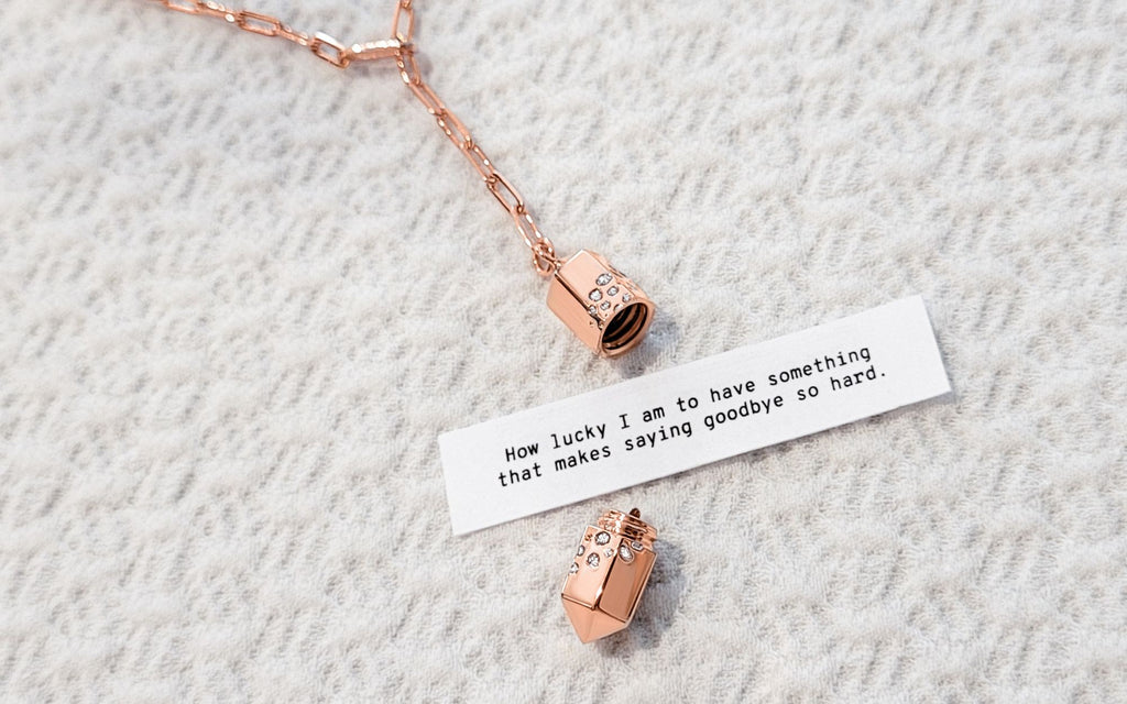 Open rose gold polygon lariat locket with fortune over a white textured background.