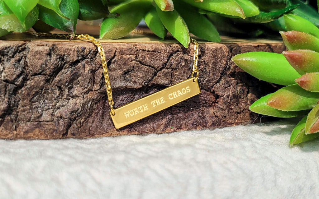 "Worth the Chaos" engraved gold pendant in front of wood and succulents
