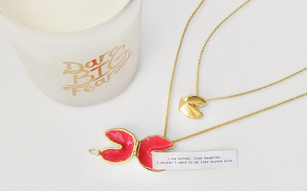 A candle and a flat lay of Fortune Cookie necklaces with fortune.