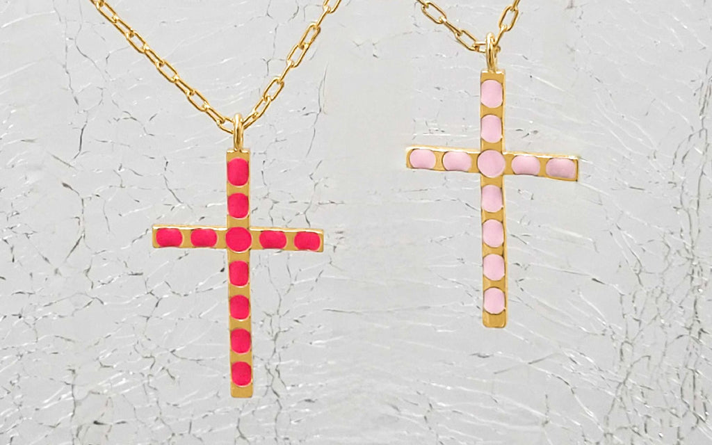 A blush and pink cross pendants over textured glass.