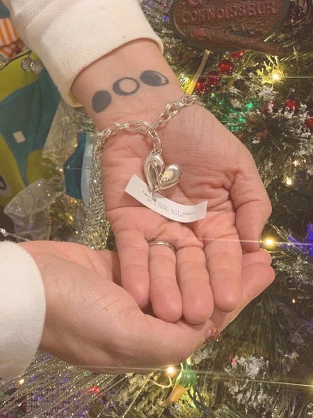 Two hands holding a Heart + Arrow bracelet with an open fortune.