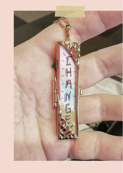 Shown Here: Julie's hand holding her locket necklace with a colorful fortune, featuring the word "Change" positioned vertically down the middle.