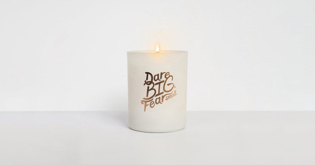 A "Dare BIG. Fear small." candle lit over a white background.