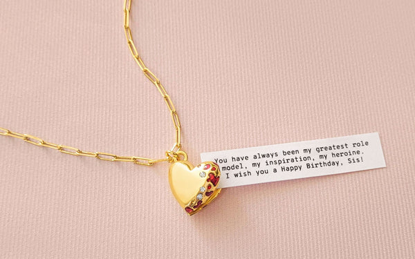 Jewelry heart locket opened to show a fortune message coming out of it over a peach background.