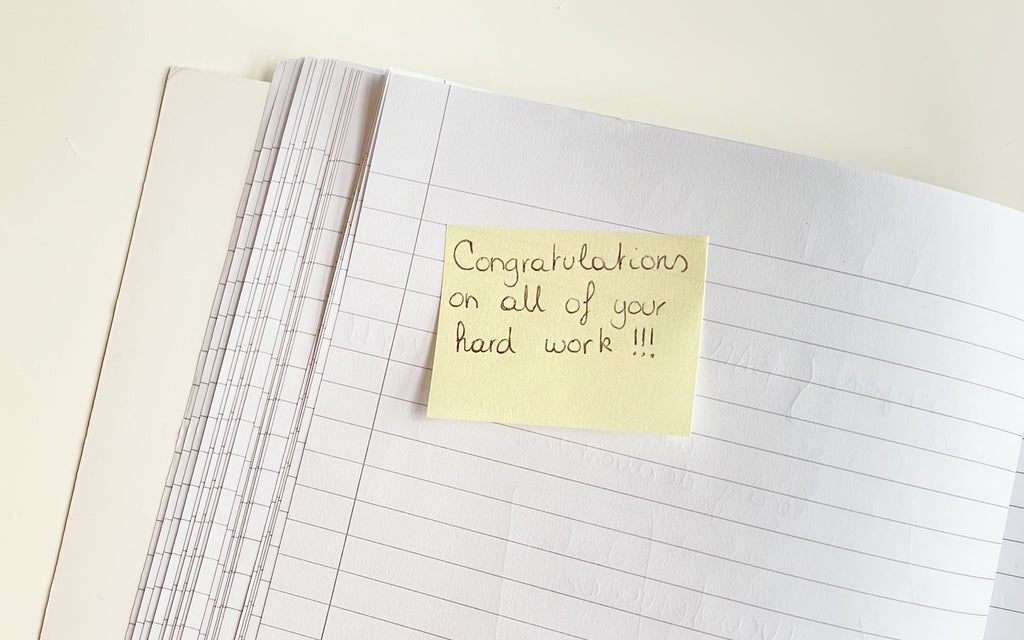 A notebook with a post-it note that reads "Congratulations on all of your hard work!"