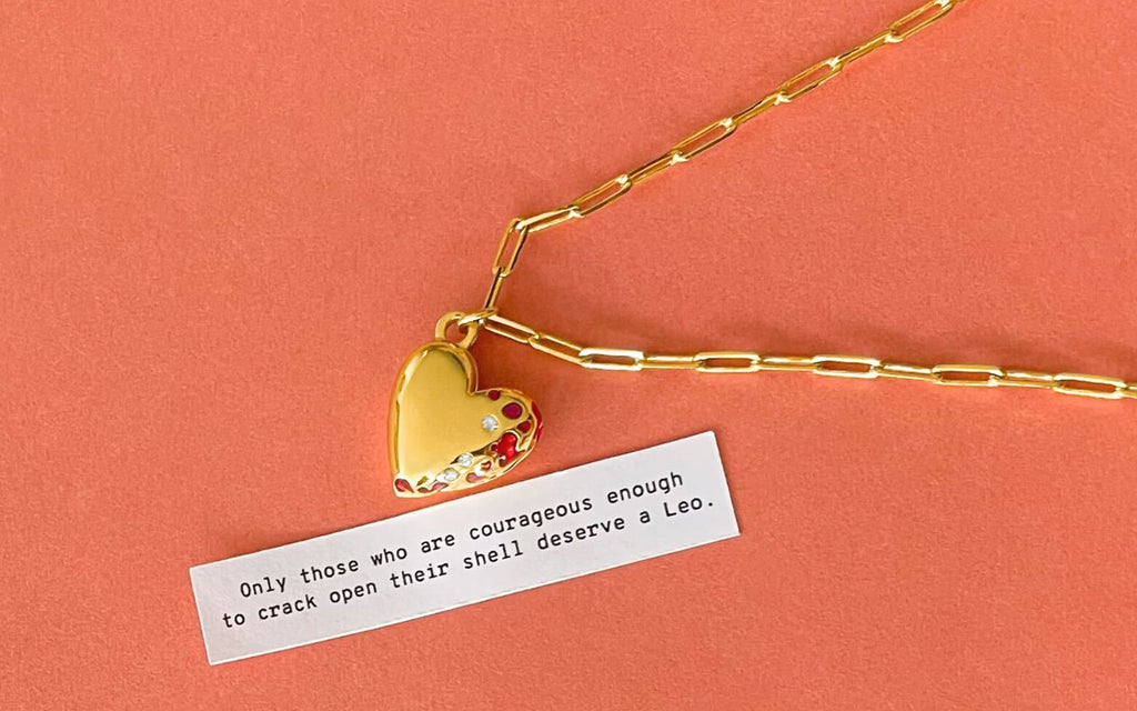 Jeweled heart locket with a fortune over an a slight orange background.