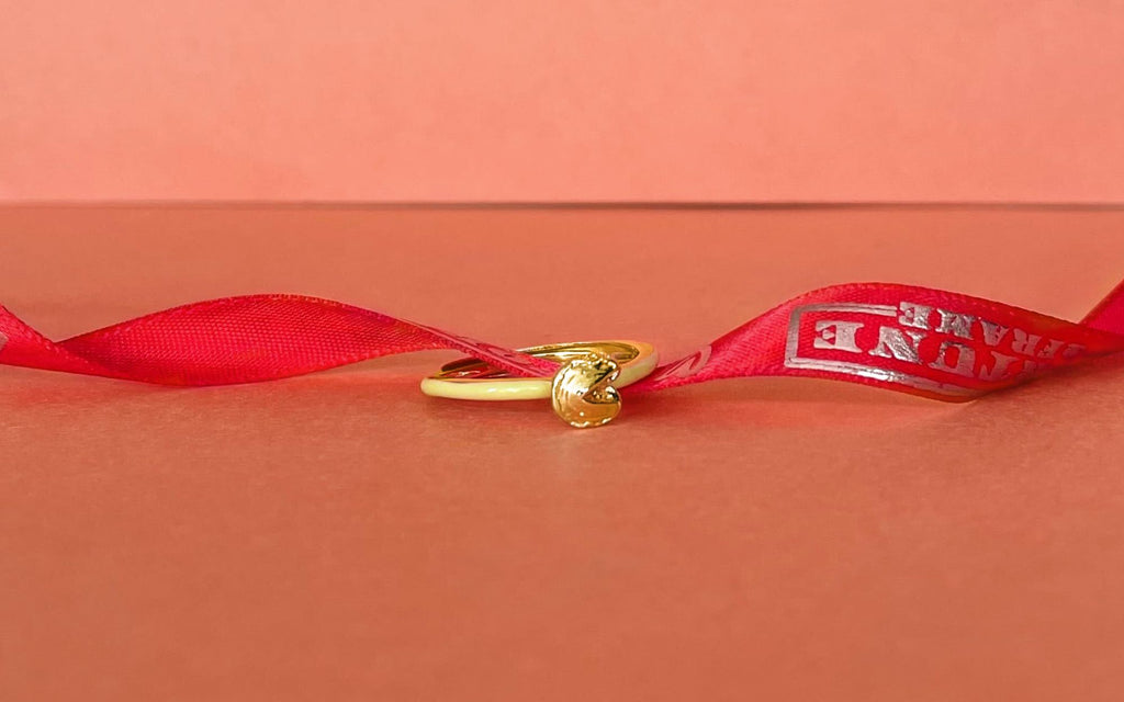 Yellow fortune cookie ring with a red ribbon through it over a slight orange background.