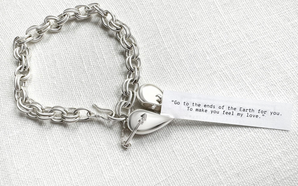 Silver Heart + Arrow Bracelet slightly opened with a fortune coming out of it that reads "“Go to the ends of the Earth for you. To make you feel my love.” On a white background.