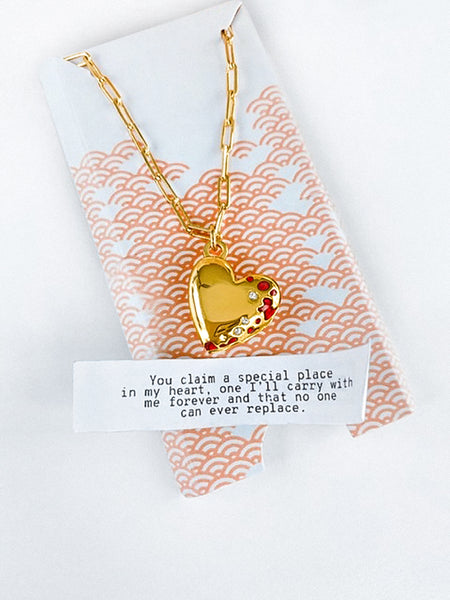 A Fortune & Frame Heart Locket Necklace with its packaging accompanied by a fortune that reads ""I can either laugh or cry... I try to always choose laughter."