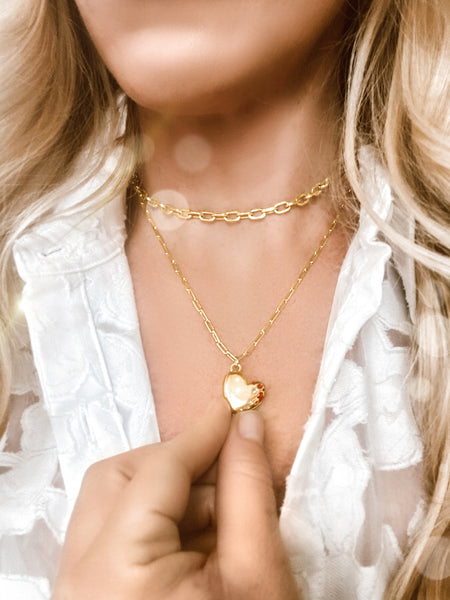 Image of a woman wearing the Fortune & Frame Heart Locket and holding it with her hand. 
