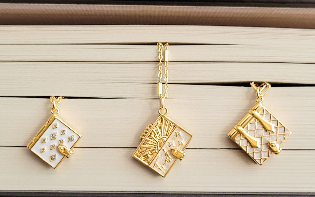 Ivory Stardust Book Locket, Trust Secret Scripture Locket, and Pearl Secret Diary Book Locket hanging from book pages