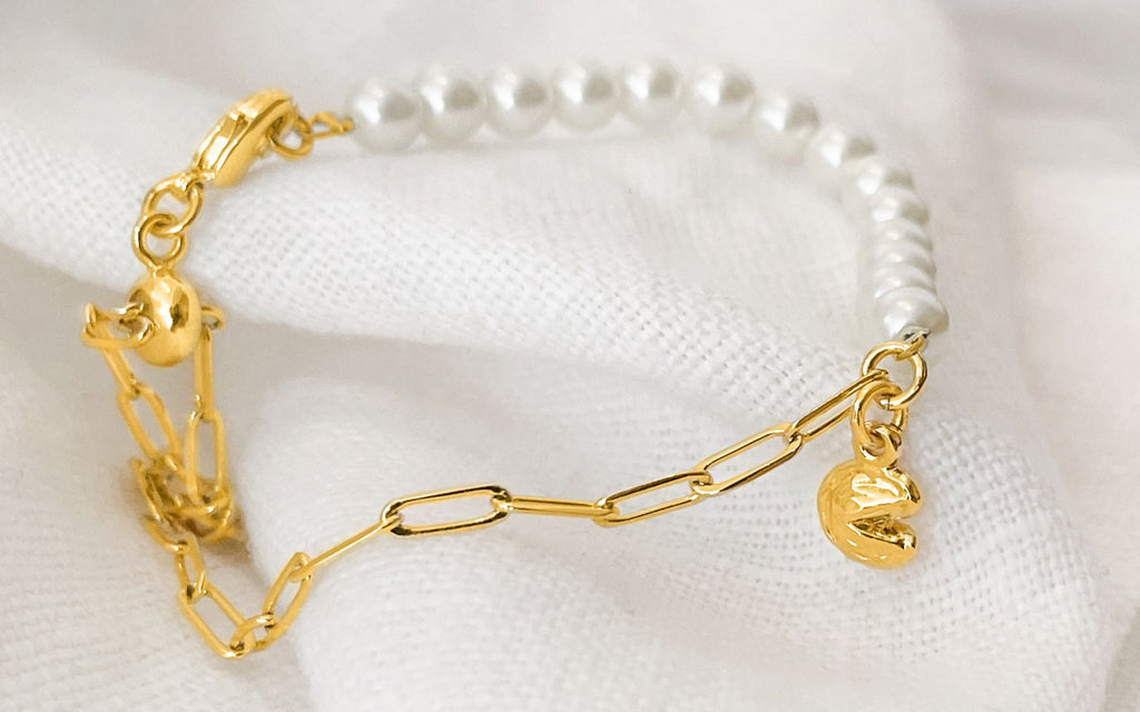 Half gold chain, half pearl fortune cookie bracelet over a white cloth.
