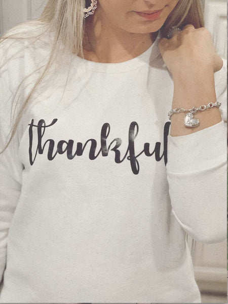 A woman wearing a white shirt with the text "Thankful" written in black.