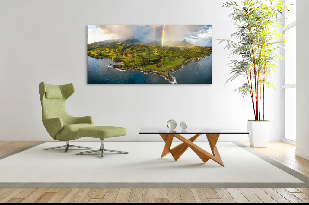 Room with photograph on the wall of Kalae Kiki Rainbow above a green chair and wood and glass coffee table with bamboo plant in corner.