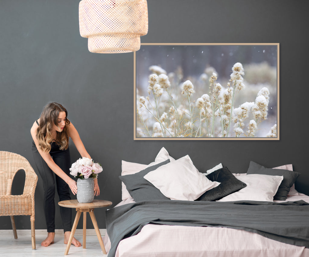 woman putting flowers on nightstand beside bed with artwork above headboard