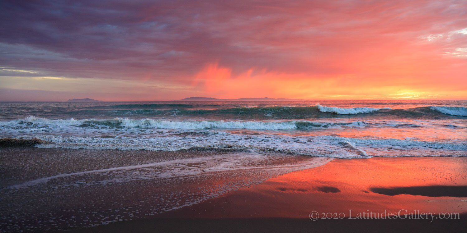 A red, orange, purple, and yellow colored coastal beach sunset over small crashing waves.