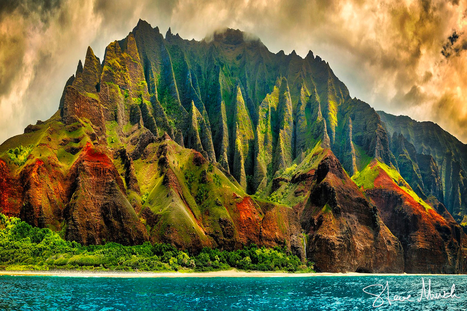 Stunning Hawaii landscape photography of soaring green and rust colored cliffs. The photograph was taken by boat off the Nā Pali Coast.