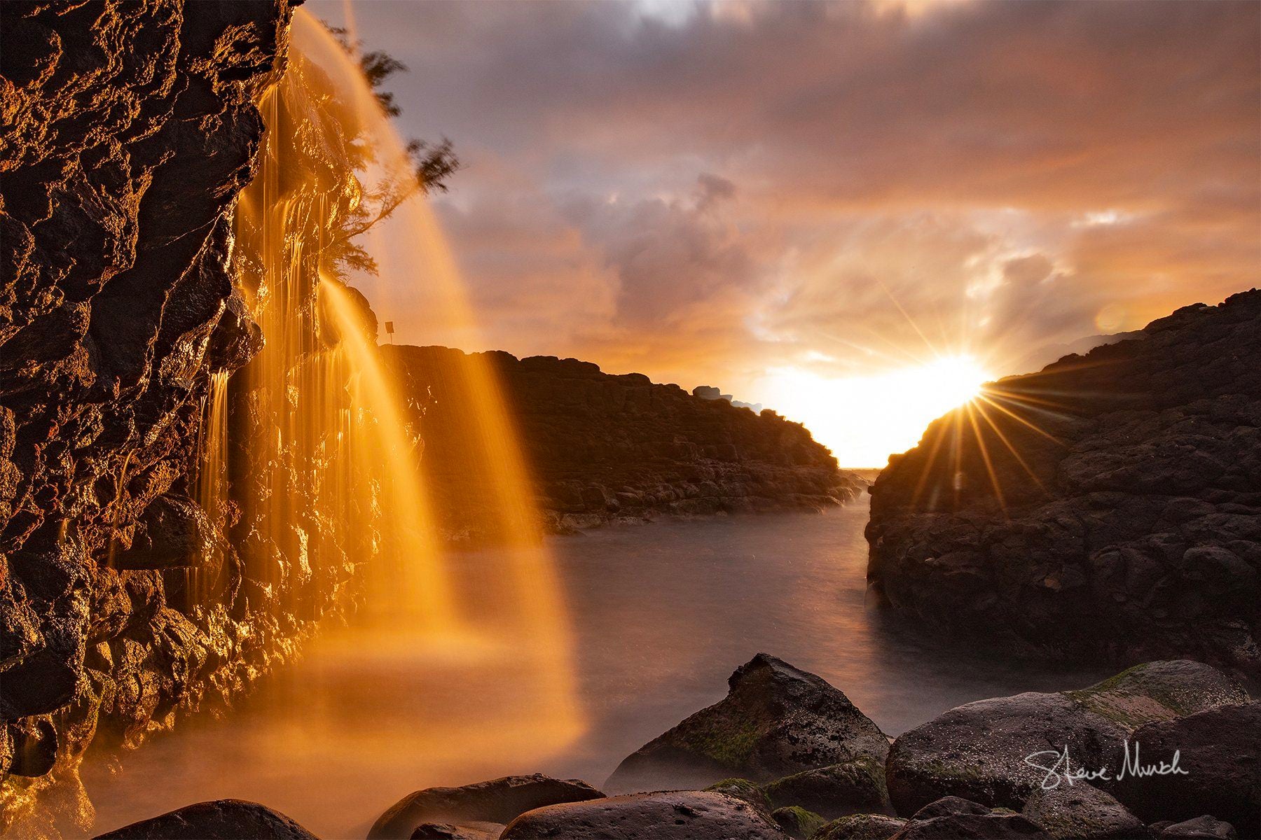 The sun hitting golden waterfalls as they feed into the waters of Kauai's North Shore.