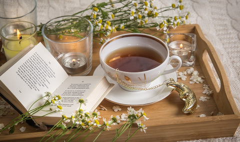 una bandeja de madera con flores, un libro y una taza de té blanco