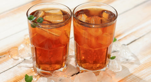 Dos vasos de bebida fría hecha con té verde con frutos rojos y hojas de hierbabuena