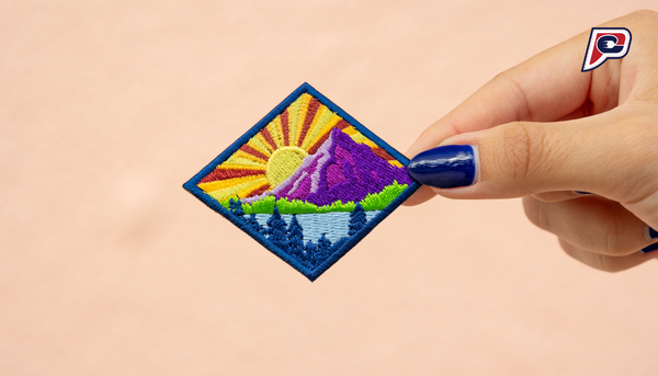 "Holding the 'Call of the Wild' embroidered iron-on patch in front of a vibrant pink wall, showcasing a captivating mountain scene art patch with intricate detailing."