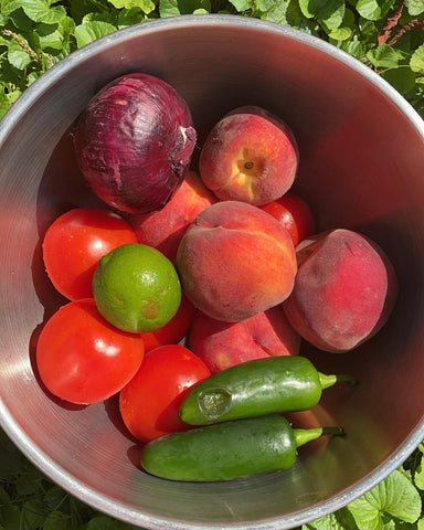 Peaches, tomatoes, jalapeños, onion, and lime in a metal mixing bowl.