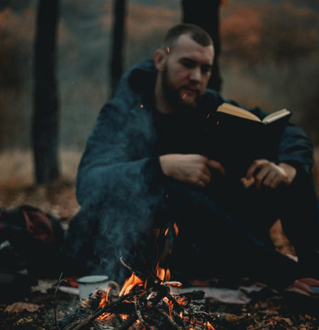 Man reading a book by a campfire