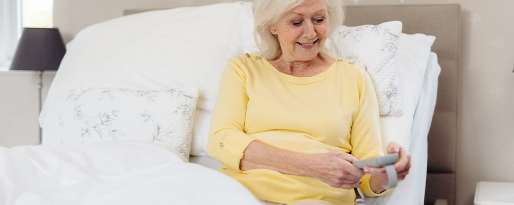 Elderly woman in yellow top sat up in bed holding a remote control