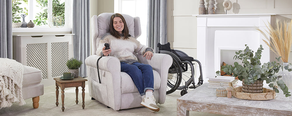 A young female sat in a recliner chair smiling holding the hand control