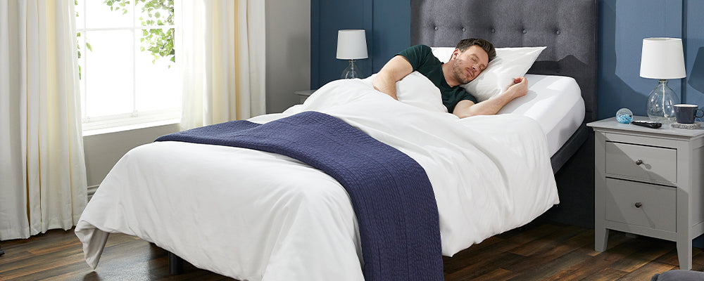 Young man with brown hair sleeping in an adjustable bed with the back-rest raised and his arm under the pillow.