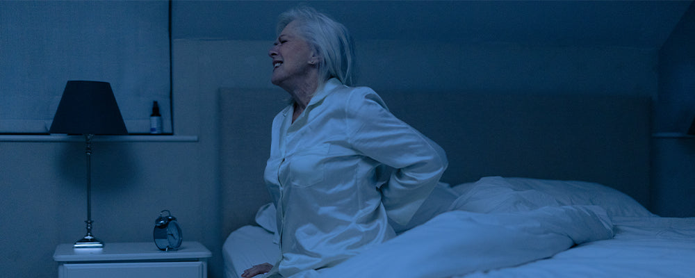 A older woman sat at the end of the bed n the middle of the night holding her back