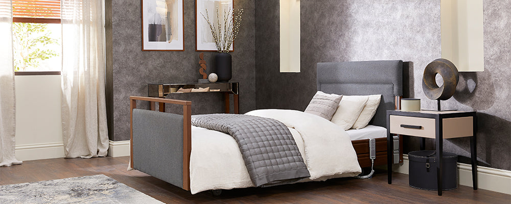 A walnut wooden profiling bed with dark grey upholstered headboard in a bedroom with cream coloured bedding and cushions on the bed