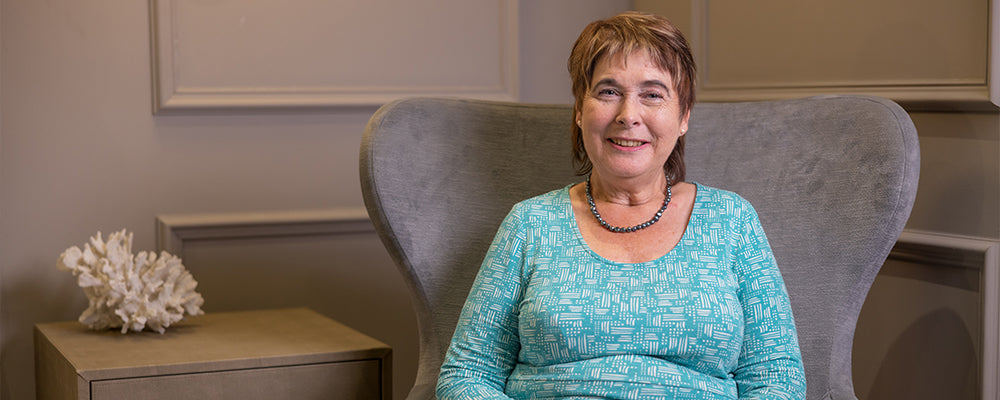 Woman with short brown hair wearing a blue dress sat in a winged back chair