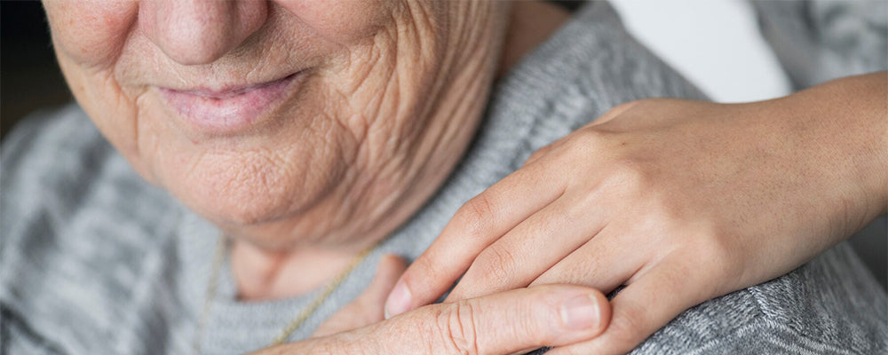 A close up of an elderly person touching hands with someone on their shoulder