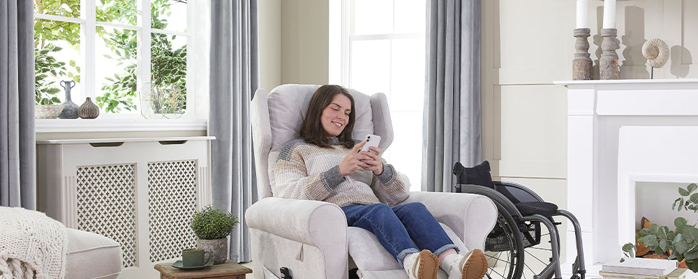 A younger female with brown hair sat in a riser recliner chair with her legs up on her mobile phone