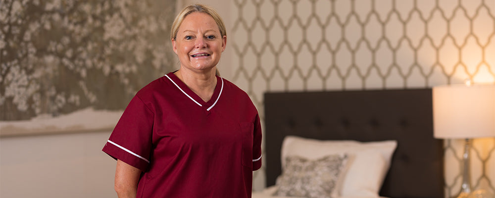 A woman with blonde hair smiling wearing a healthcare tunic