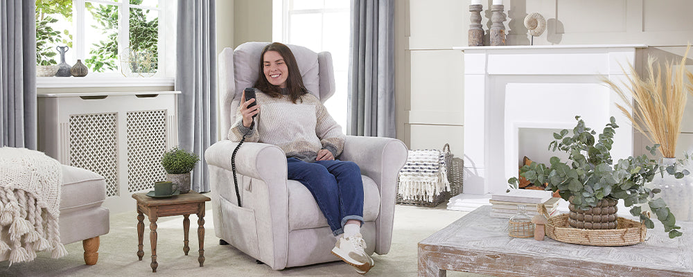 A younger female with brown hair sat in a riser recliner chair holding the wired hand control